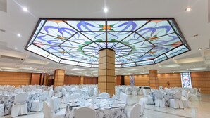 A banquet hall with round tables set for events, a large stained glass ceiling, and a central wooden pillar. - Hotel Abades Loja (Loja)