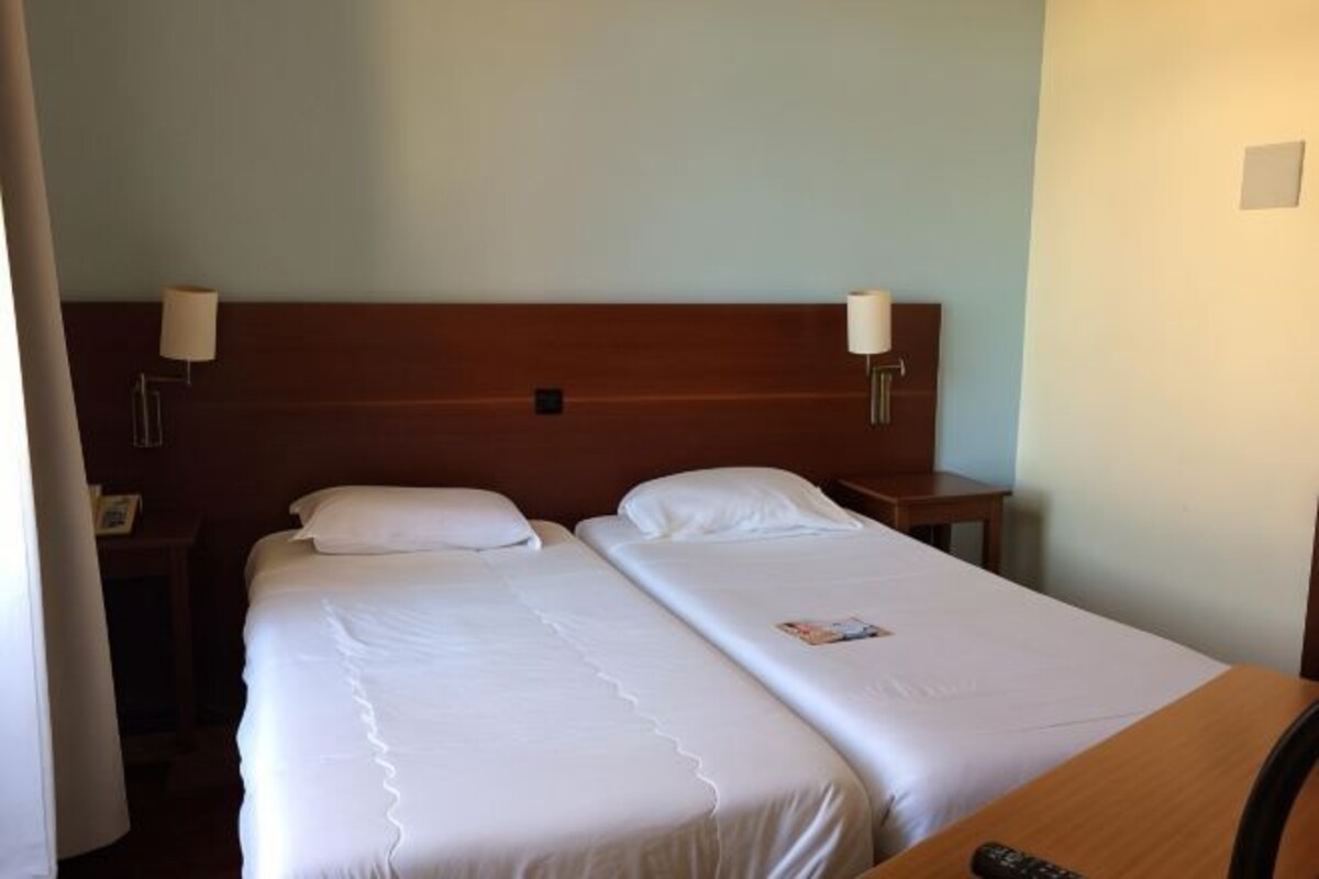A hotel room with two single beds, a wooden headboard, bedside lamps, and a nightstand.