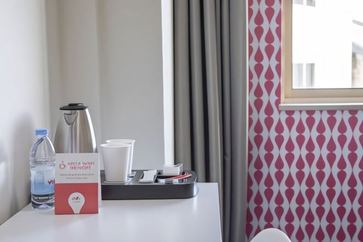 A hotel room with a table set with a water bottle, a box of tissues, and a tray with cups and a thermos.