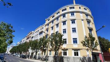 A multi-story hotel with a curved facade, balconies, and a parking area with cars.