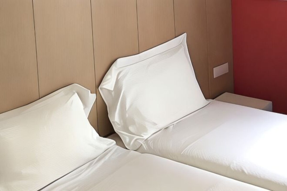 Two beds with white linens in a room with wooden paneling and a red accent wall.
