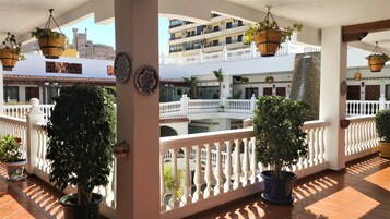A multi-level outdoor terrace with potted plants, white balustrades, and a view of a building with balconies.