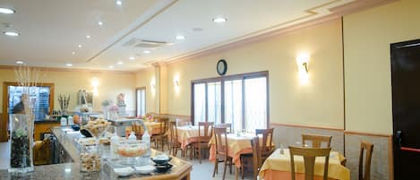 A dining area with multiple tables and chairs, a buffet counter with various food items, and a clock on the wall.