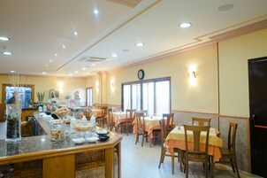 Un comedor con varias mesas y sillas, una barra de buffet con diversos alimentos y un reloj en la pared.