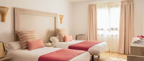 Habitación de hotel con dos camas, cabecera de madera, mesita de noche, lámpara y ventana con cortinas.