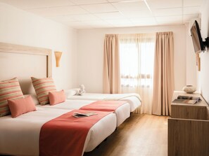 A hotel room with two beds, a wooden desk, a vase, and a television on the wall.