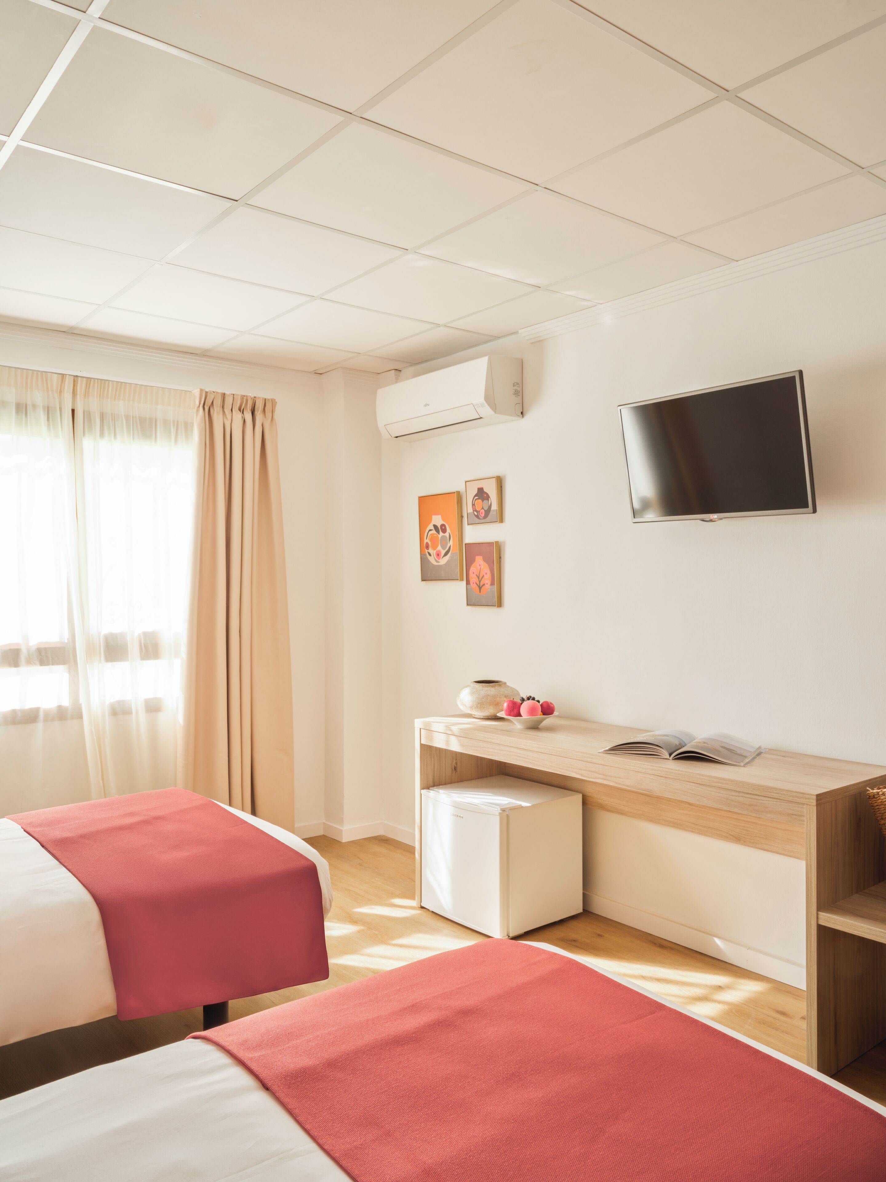 Una camera d'albergo con due letti, una scrivania con un computer, una televisione e opere d'arte appese al muro.