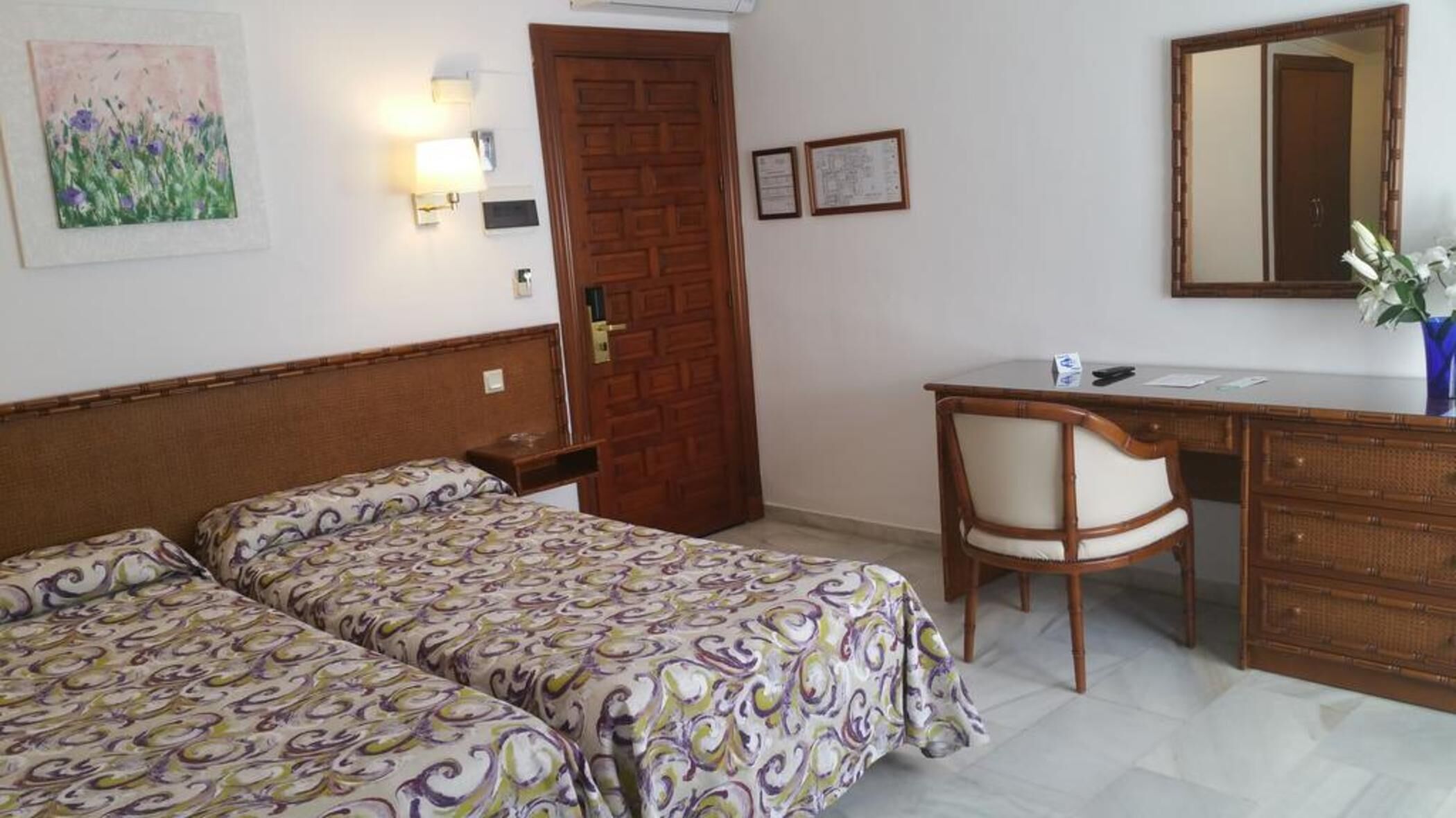A room with two beds, a desk, a chair, a mirror, and a door.