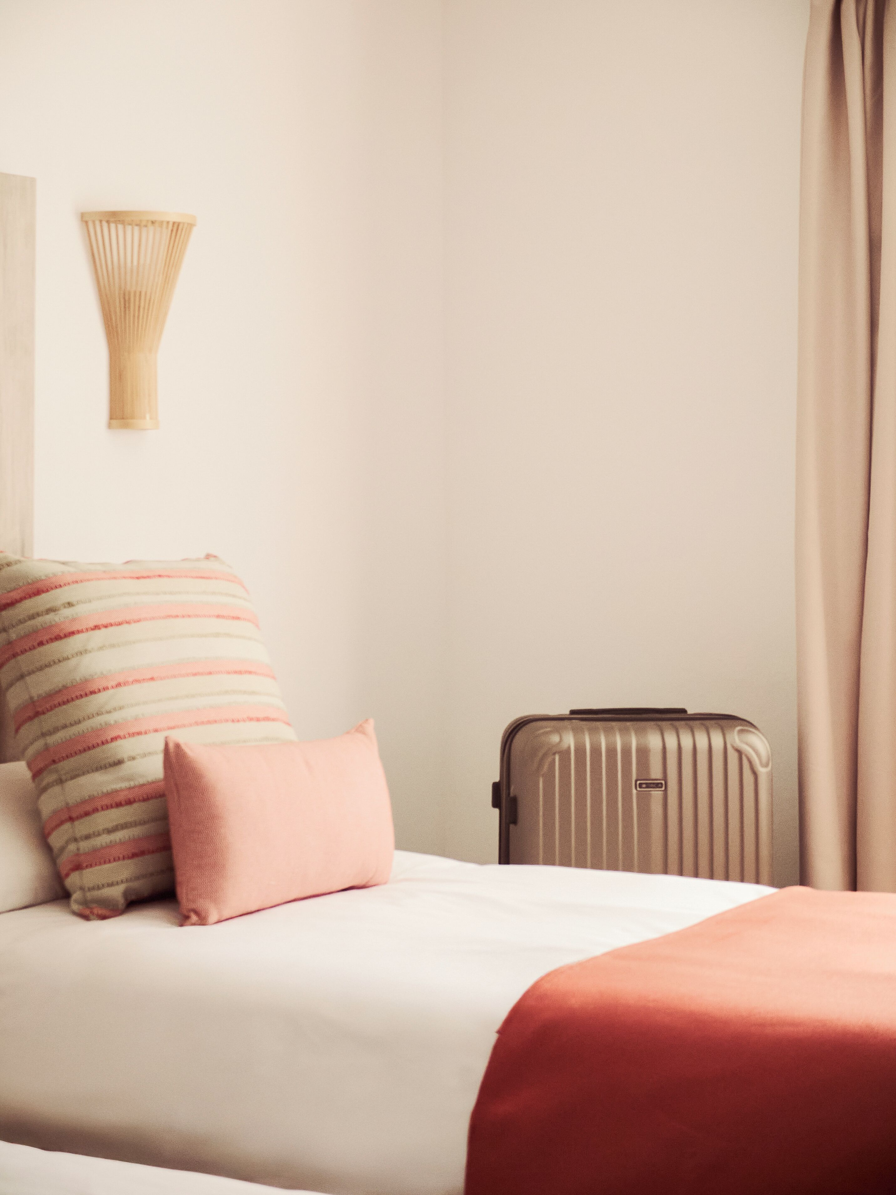 Una cama bien hecha con almohadas a rayas y una maleta en el suelo.
