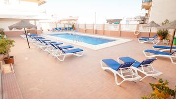 Un área de piscina en la azotea con sillones reclinables azules, una piscina y plantas en macetas.