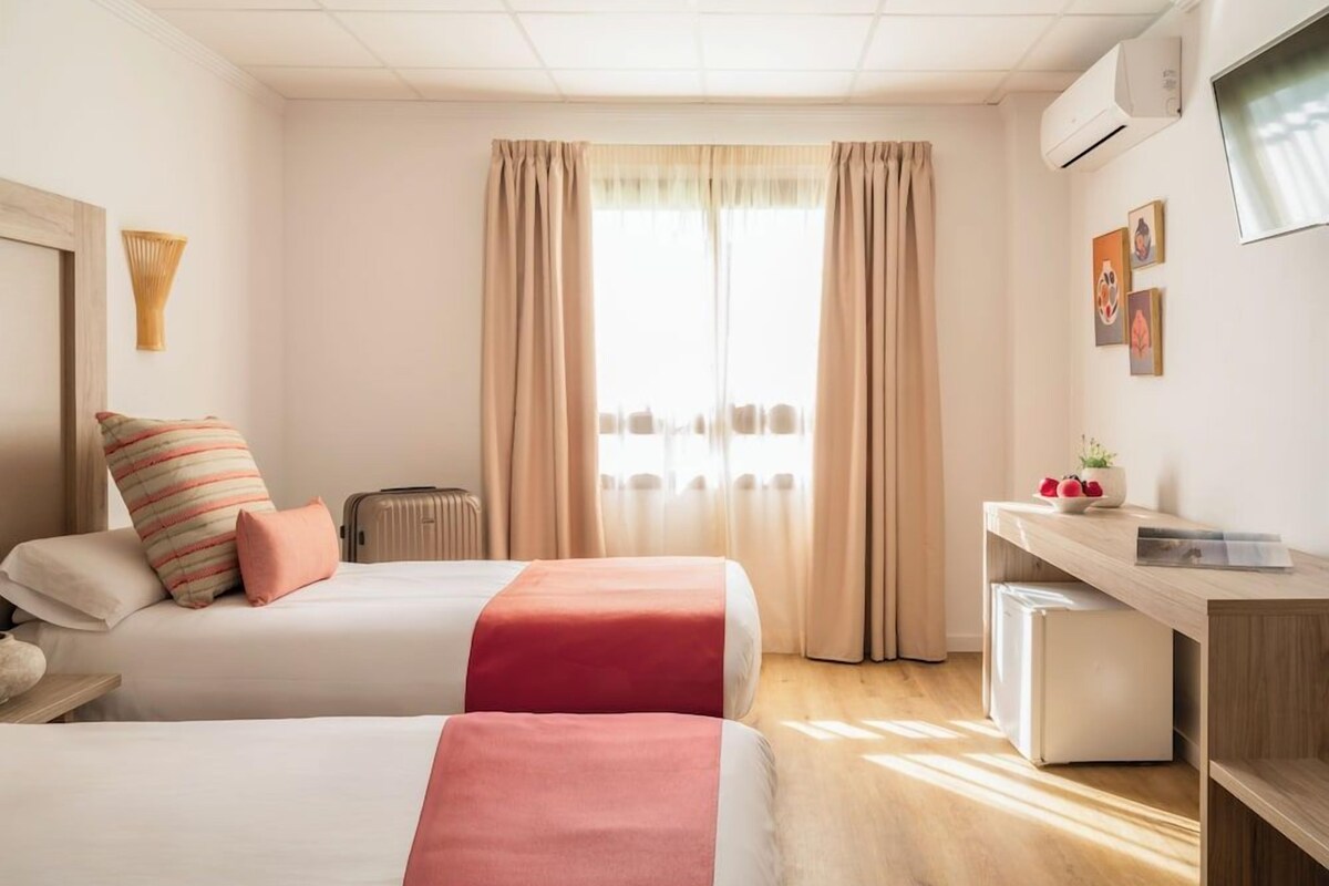 Una habitación de hotel con dos camas, un escritorio, un radiador y un televisor en la pared.