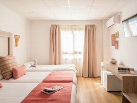 A hotel room with two beds, a desk, a small refrigerator, and a window with curtains.