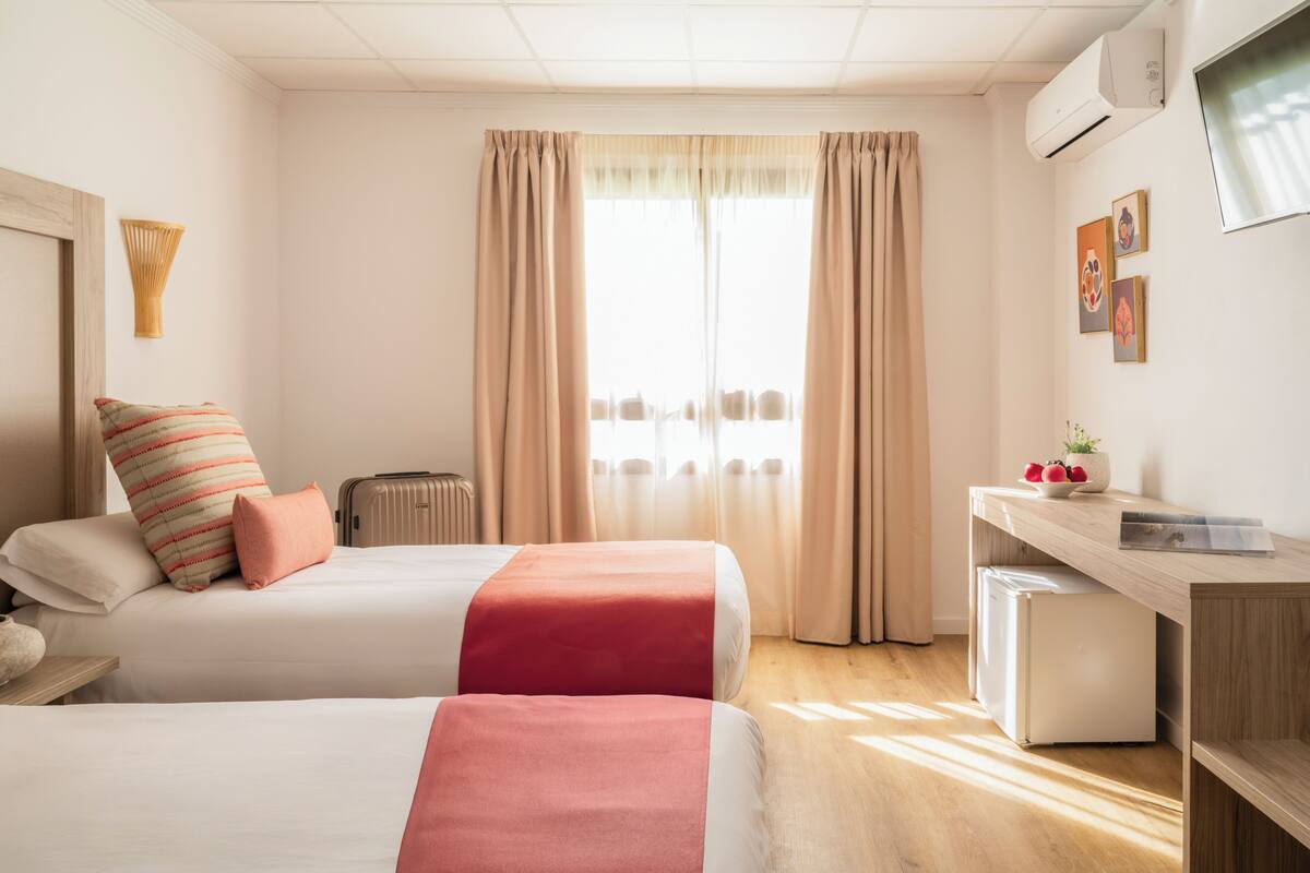 Une chambre d’hôtel avec deux lits, un bureau, un petit réfrigérateur et une fenêtre avec des rideaux.