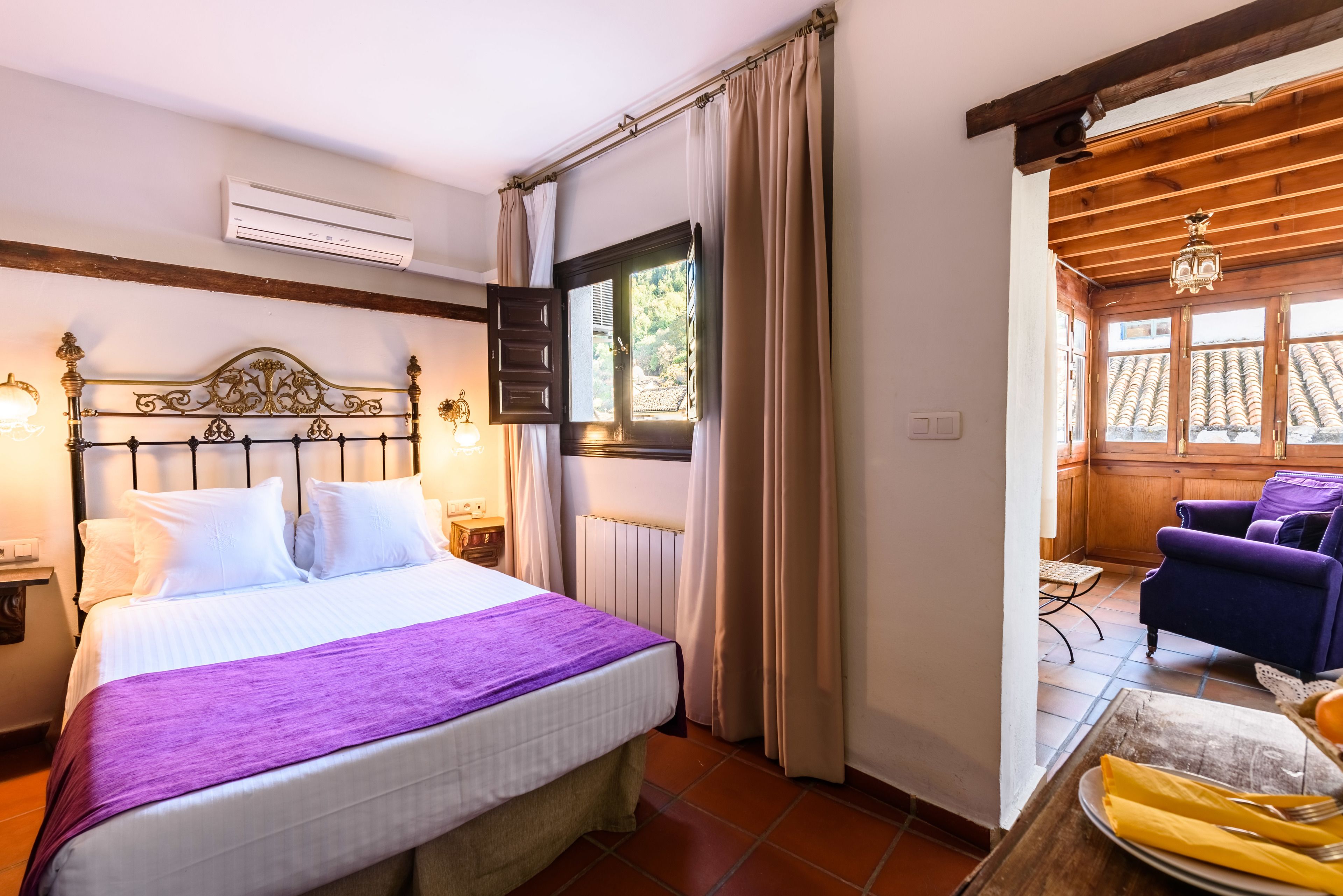 A bedroom with a bed, a window with curtains, a wooden ceiling, and a view of the outside.