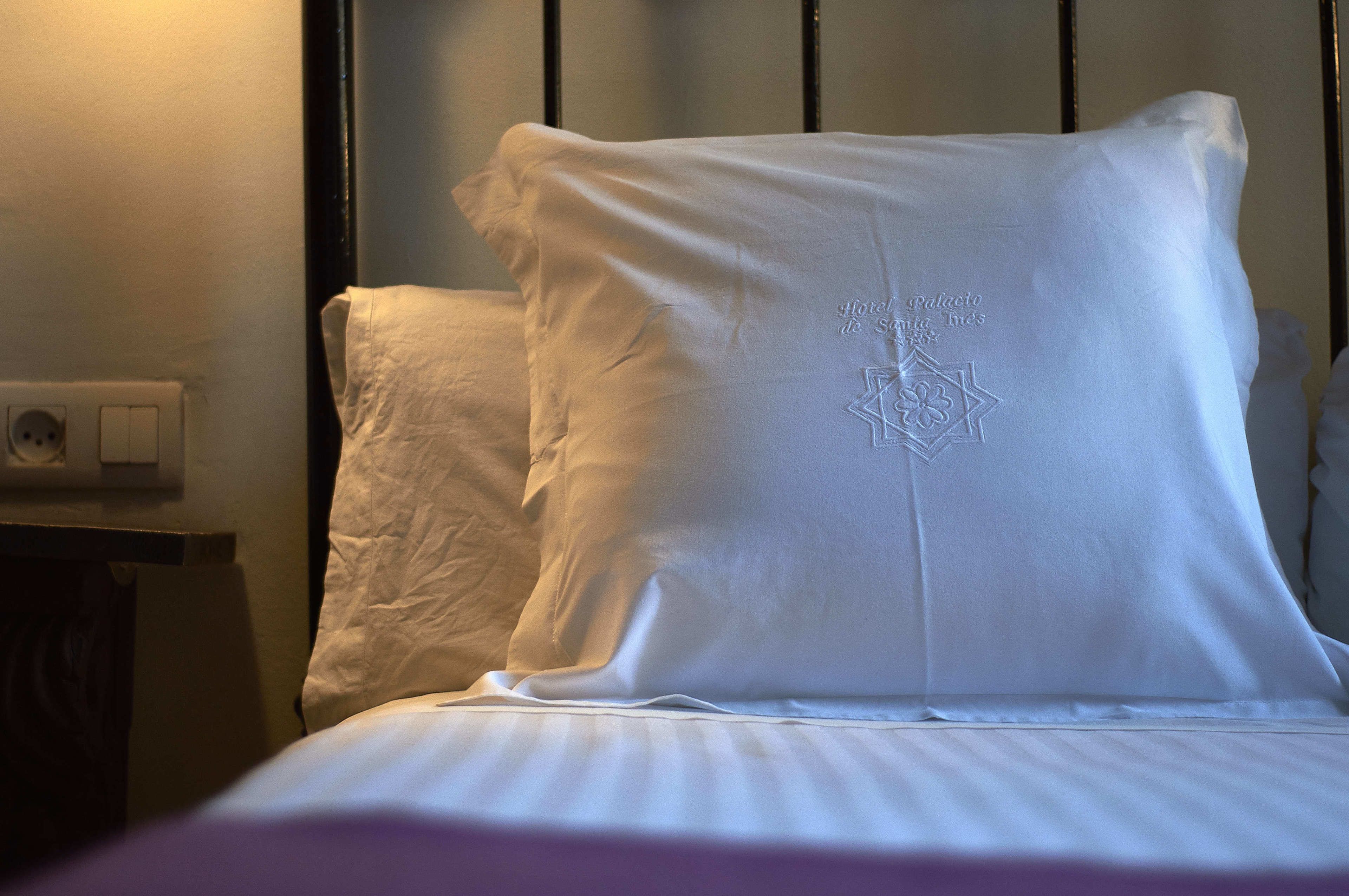 Una cama con sábanas y almohadas blancas, un enchufe y un interruptor en la pared.