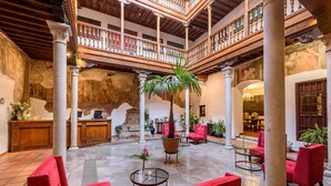 A spacious lobby with red seating, a central palm tree, and a balcony with wooden railings. - Palacio de Santa Inés hotel (Granada)