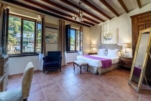 A bedroom with a bed, bedside table, lamp, chair, and a large window with curtains.