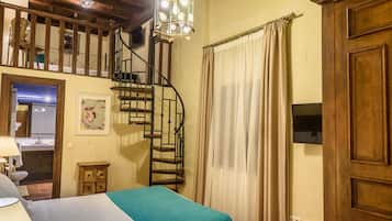 Un dormitorio con cama, una escalera de madera, una araña, un baño y una puerta grande de madera.