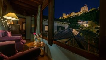 Una habitación con vistas a un castillo en una colina, techo de madera y una mesa con un jarrón y copas.