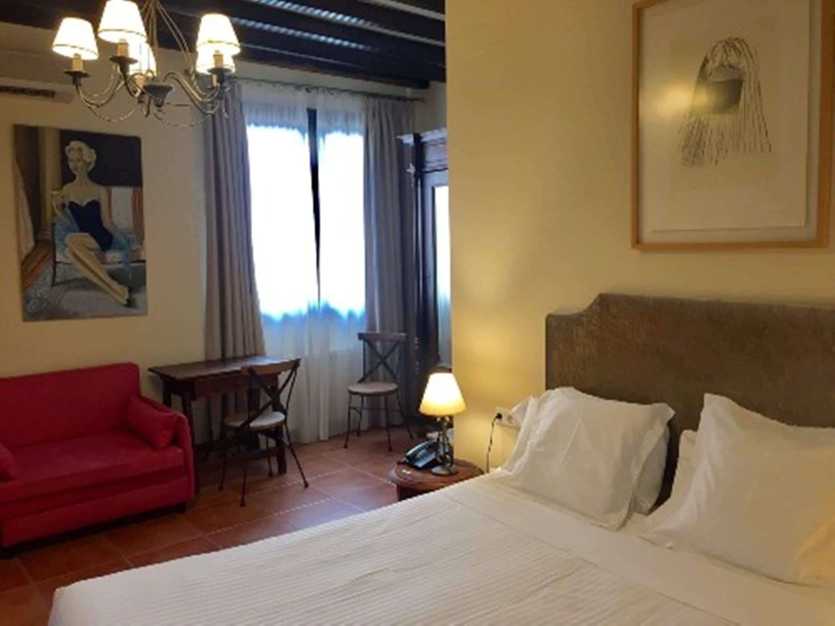 Una habitación de hotel con una cama, un sofá rojo, un escritorio con una silla y un cuadro en la pared.