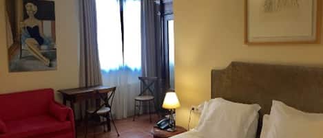 Une chambre d’hôtel avec un lit, un canapé rouge, un bureau avec une chaise et un tableau au mur.