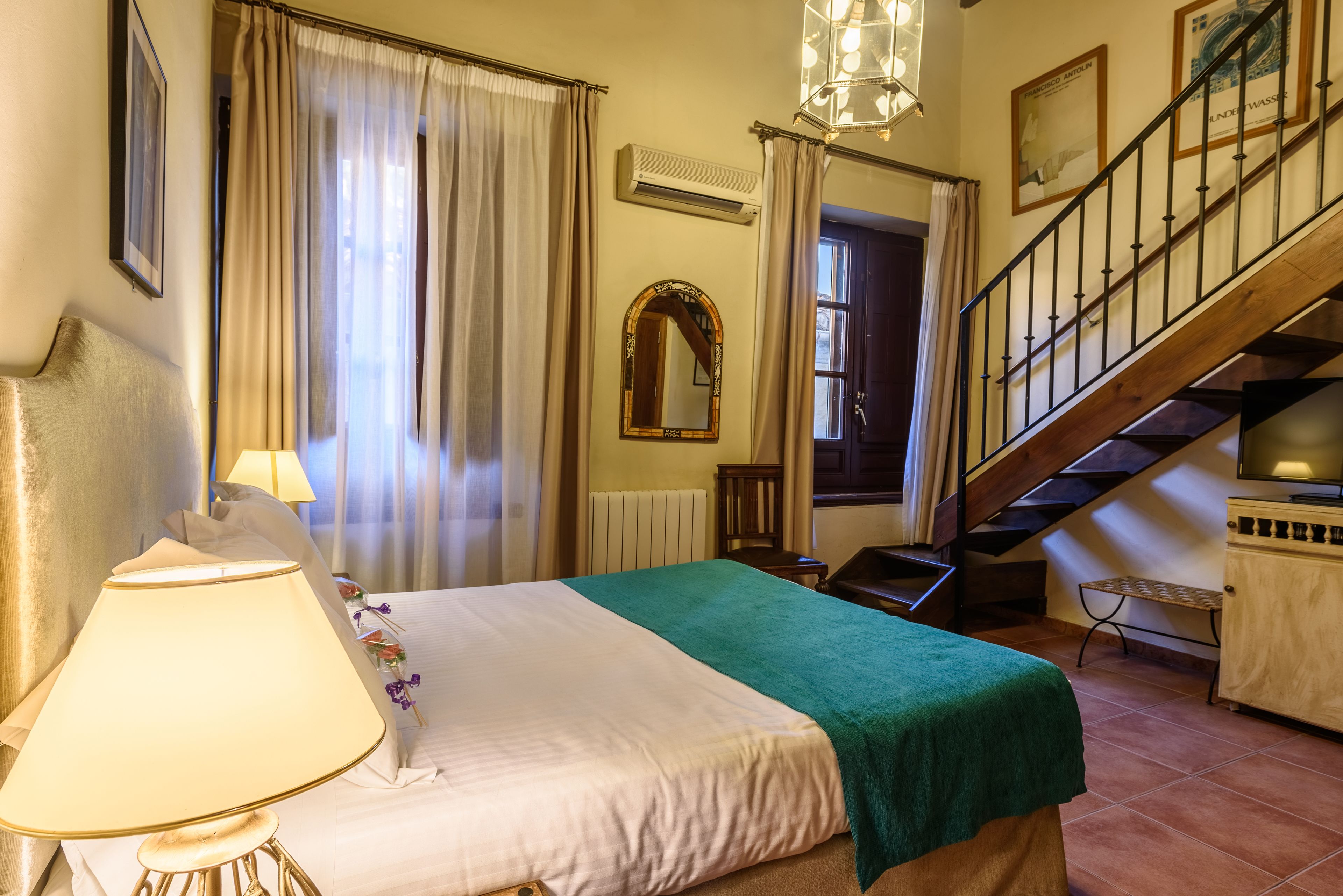 A hotel room with a bed, a lamp, a mirror, a staircase, and a radiator.