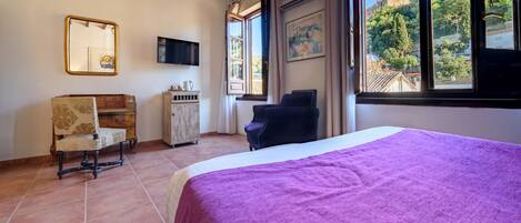 Un dormitorio con una cama grande, techo de madera, televisor, ventana con vistas a un castillo y una silla.