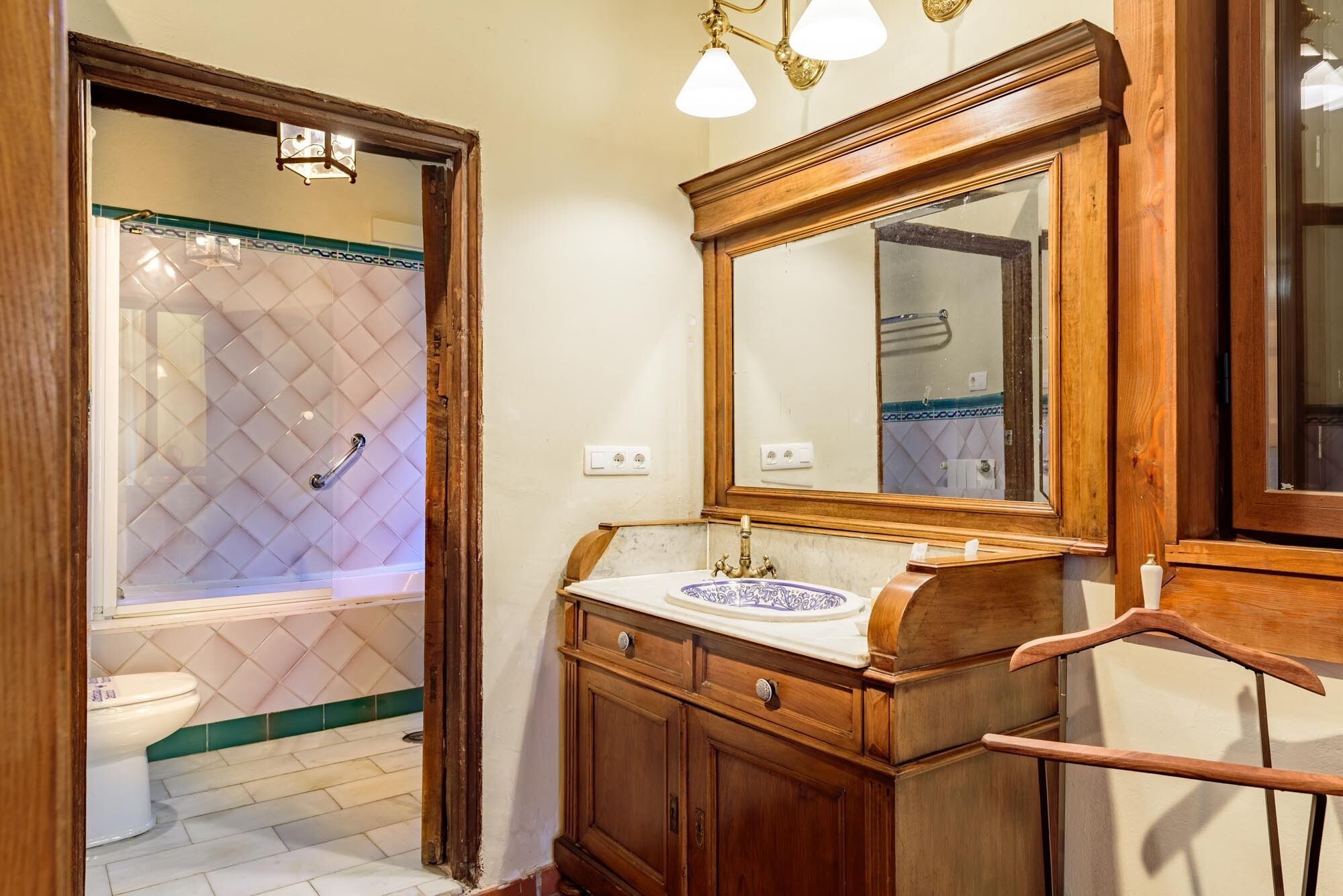 A bathroom with a wooden vanity, a large mirror, and a shower with a diamond-patterned tile wall.