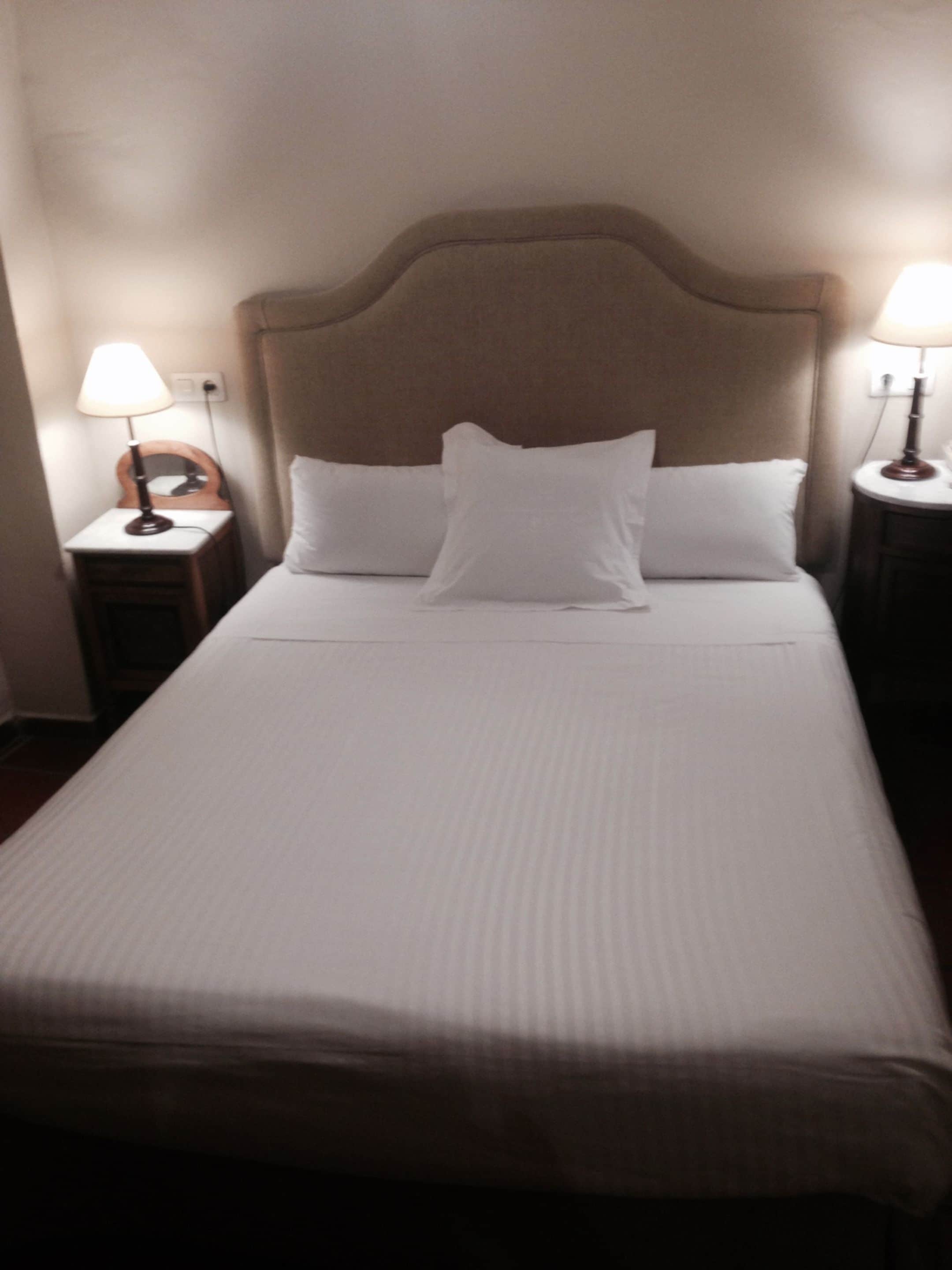 A neatly made bed with a headboard, two bedside lamps, and a nightstand.