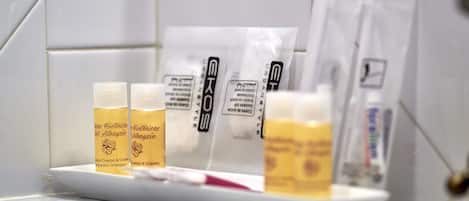Un baño con azulejos blancos, un lavamanos blanco y artículos de aseo personal, incluyendo champú y acondicionador.
