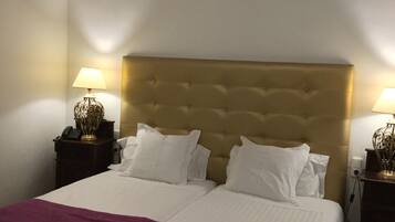 A double bed with a tufted headboard, two bedside tables with lamps, a purple throw blanket, and a woven bench.