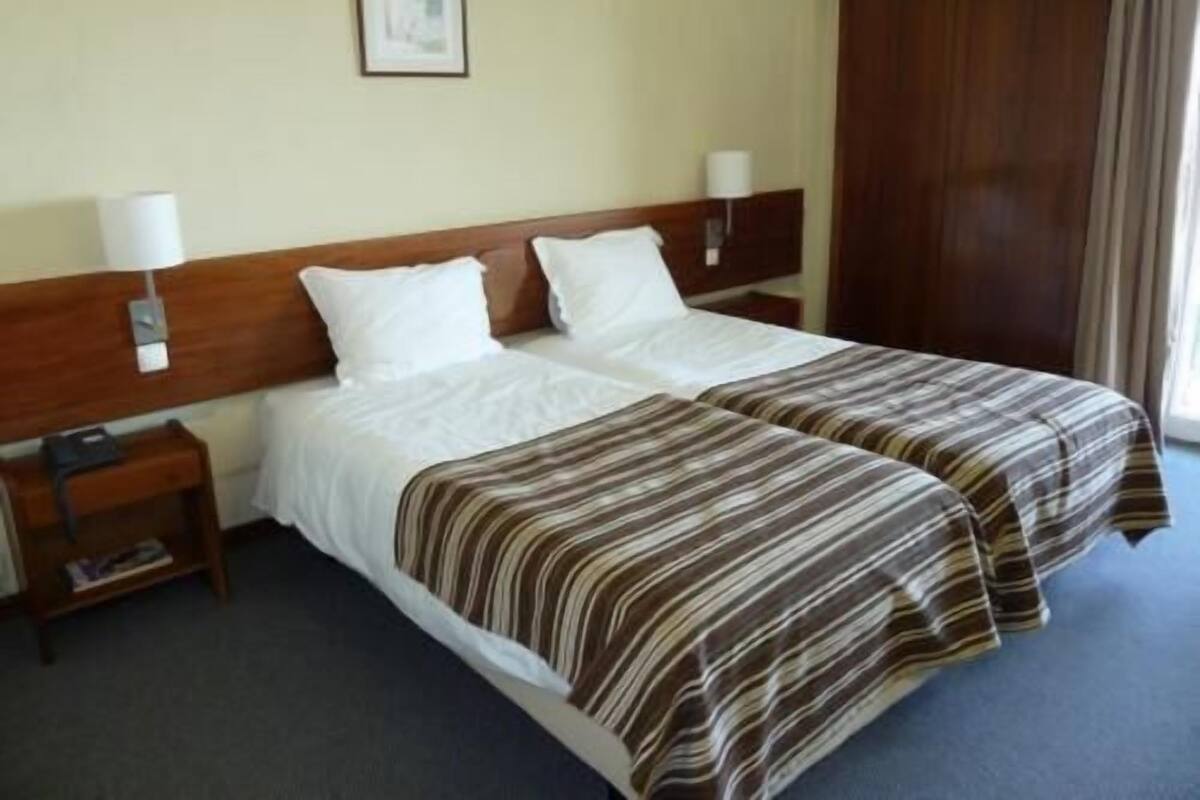 A double bed with white linens, a wooden headboard, two bedside tables with lamps, and a framed picture on the wall.