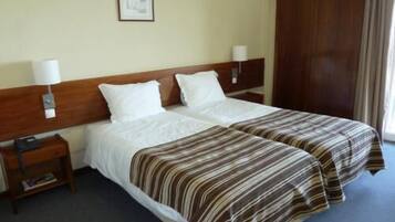 A double bed with white linens, a wooden headboard, two bedside tables with lamps, and a framed picture on the wall.