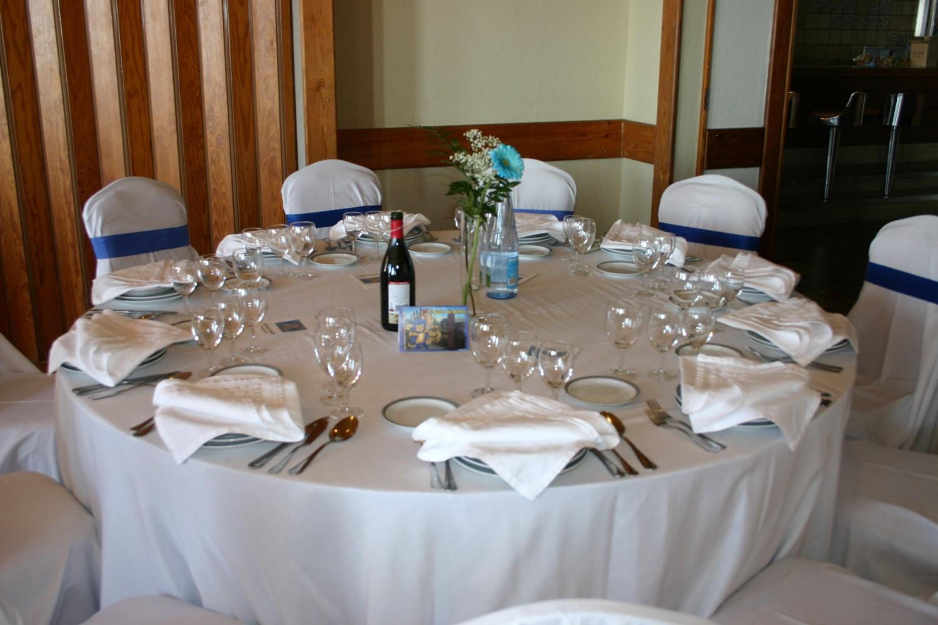 A round dining table set for a formal event, surrounded by chairs with blue sashes.