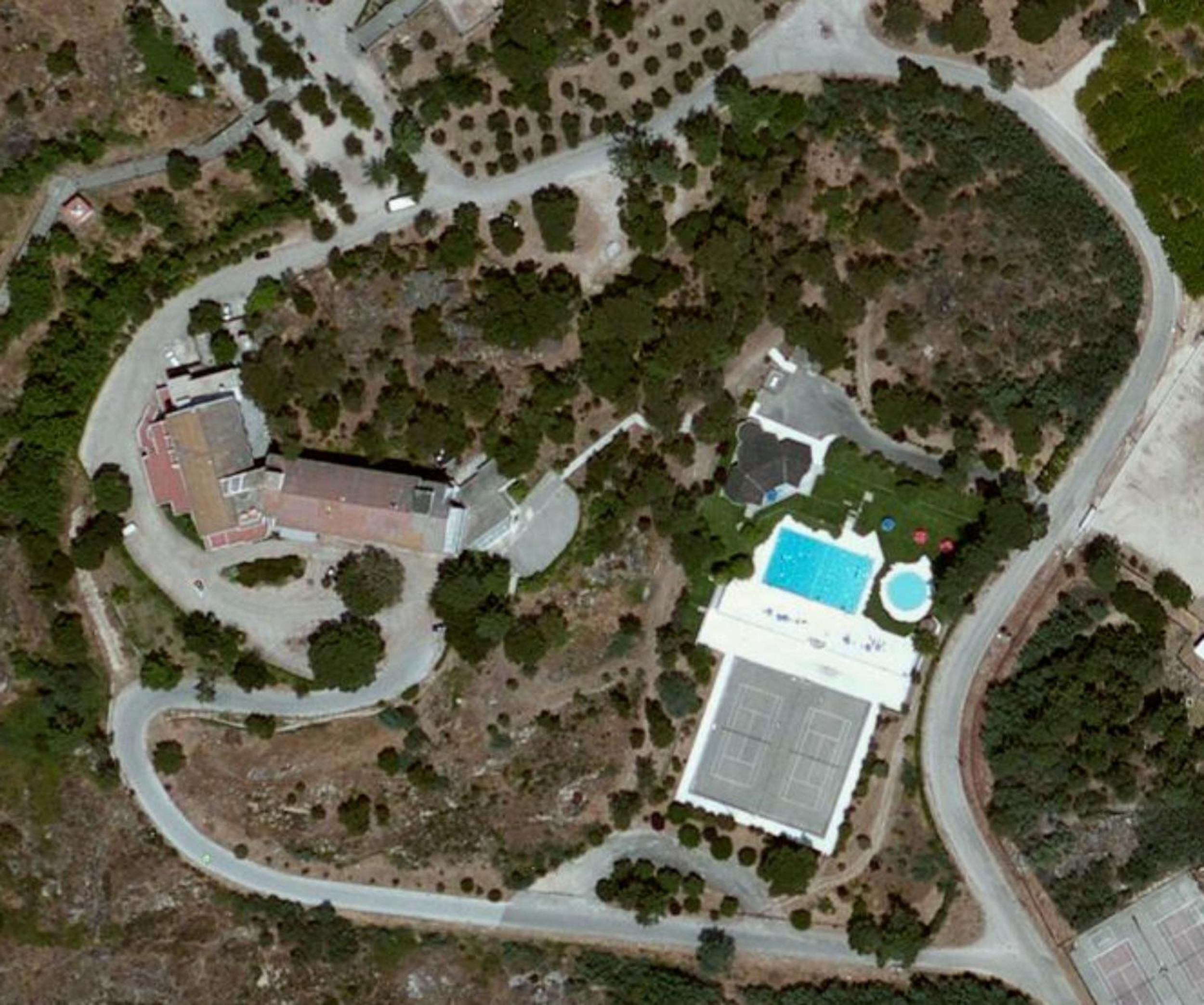 An aerial view of a property with a swimming pool, tennis court, and a building with a red roof.