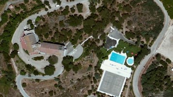An aerial view of a property with a swimming pool, tennis court, and a building with a red roof.