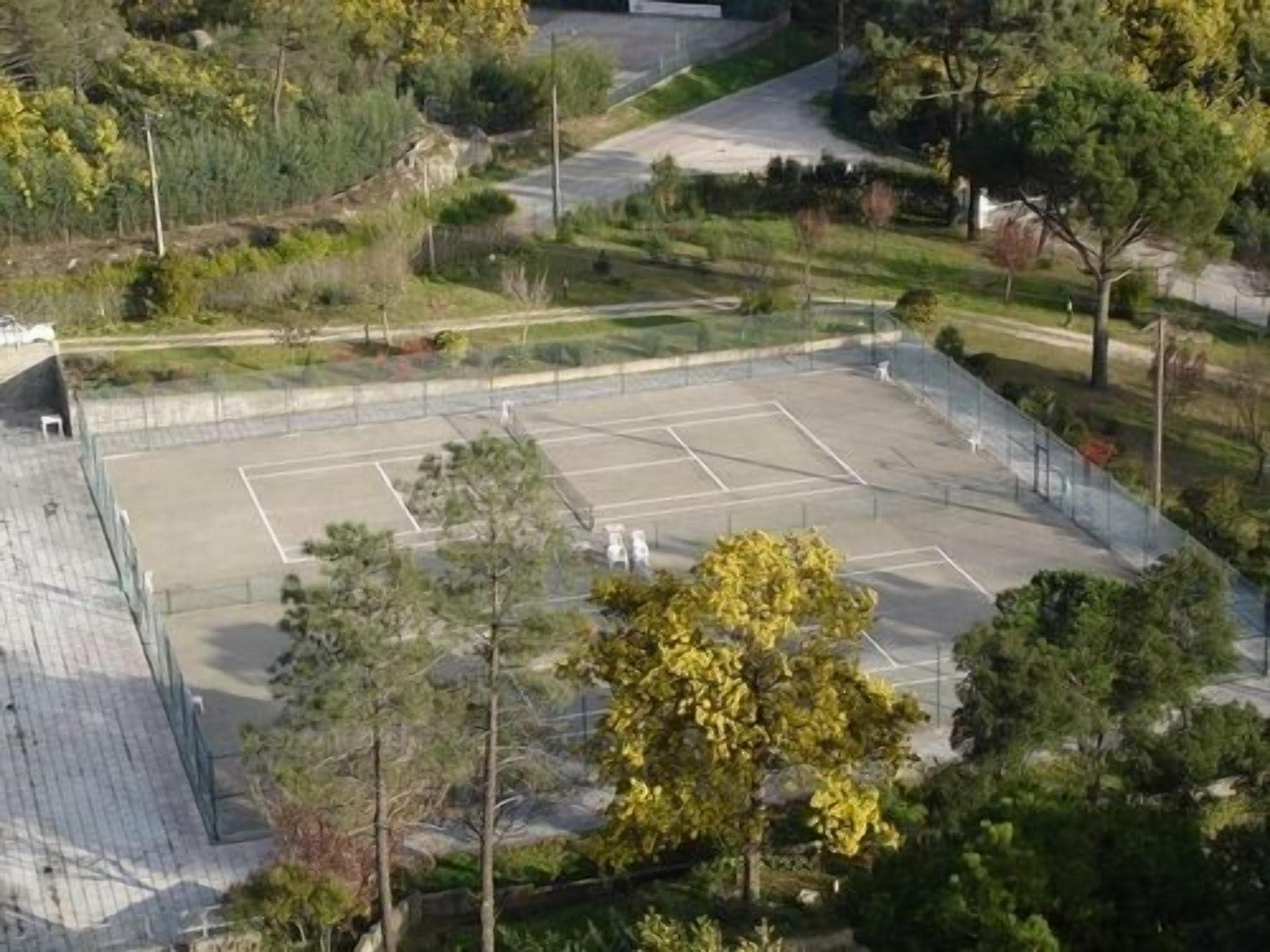 Une vue aérienne d’un court de tennis entouré d’arbres et d’une clôture.