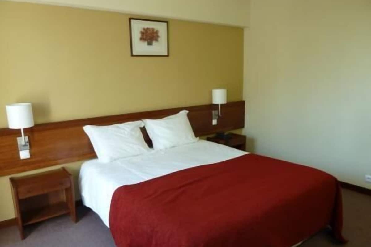 A hotel room with a bed, two bedside tables, a nightstand, a lamp, and a framed picture on the wall.