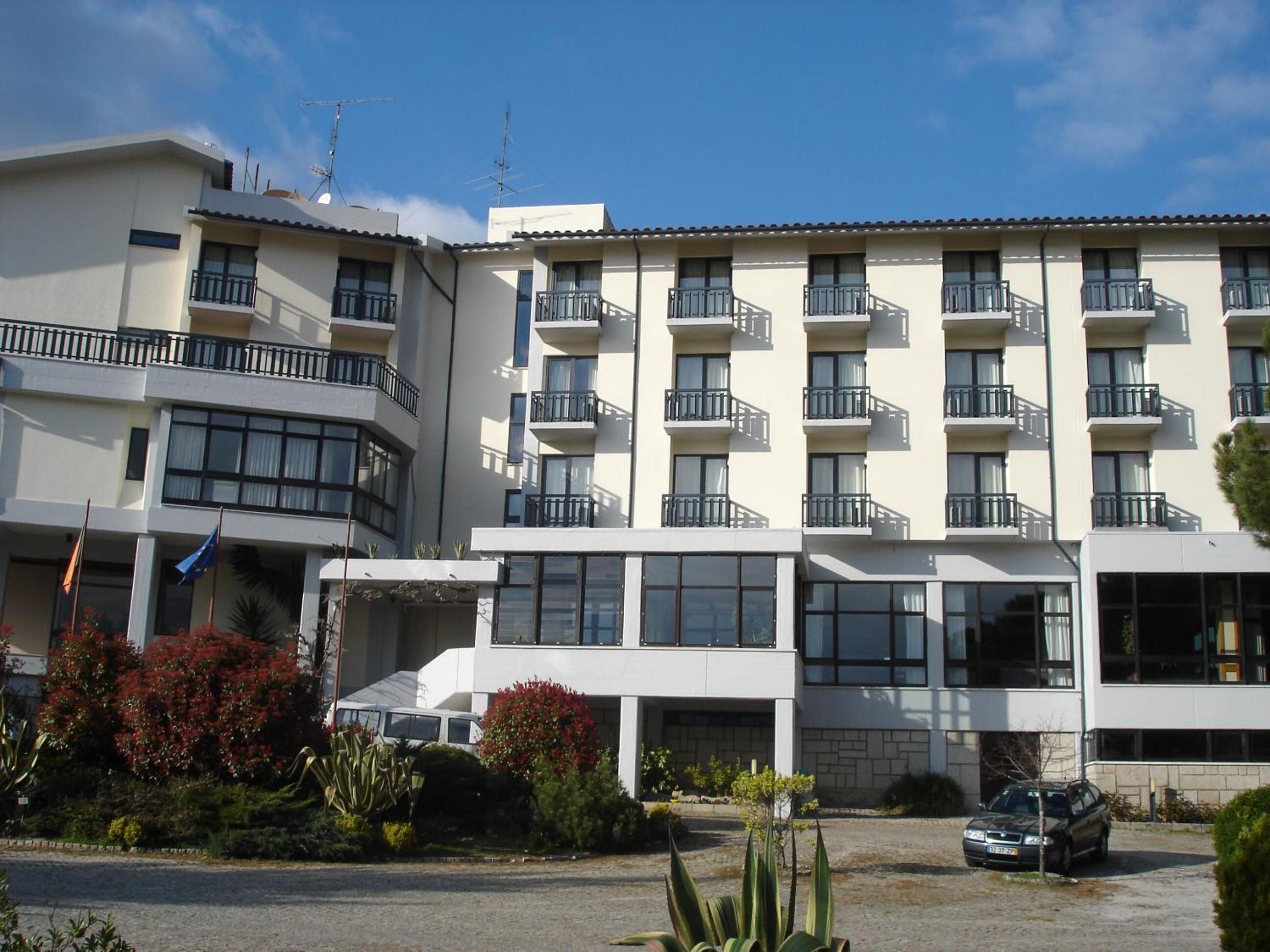 A multi-story hotel with balconies, large windows, and a parking area.