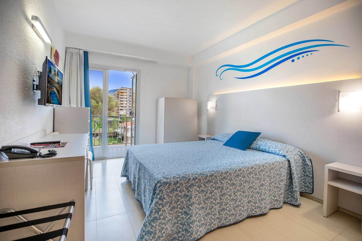 A hotel room with a bed, desk, chair, and a view of the outside.