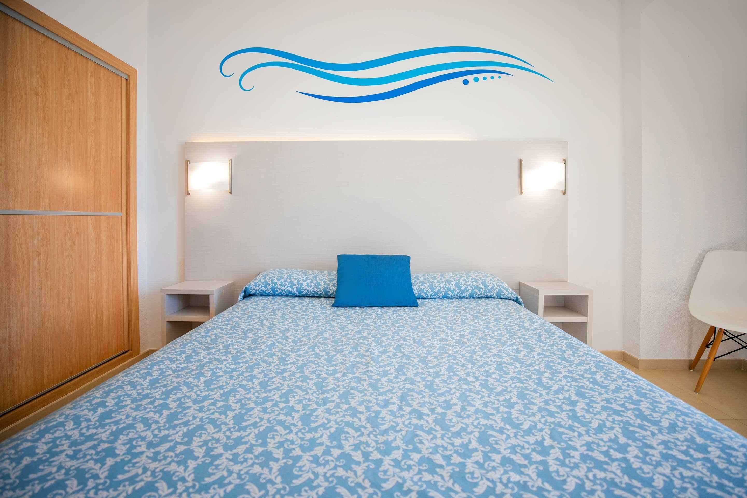 Un dormitorio con una cama grande, dos mesitas de noche, un tocador, un armario de madera y un diseño decorativo en la pared.