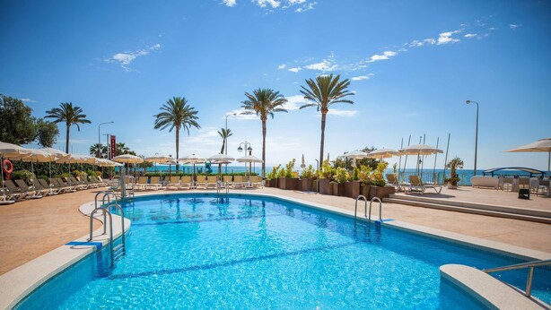 A swimming pool with lounge chairs and umbrellas, surrounded by palm trees and a clear sky. - Hotel Servigroup Trinimar (Benicassim)