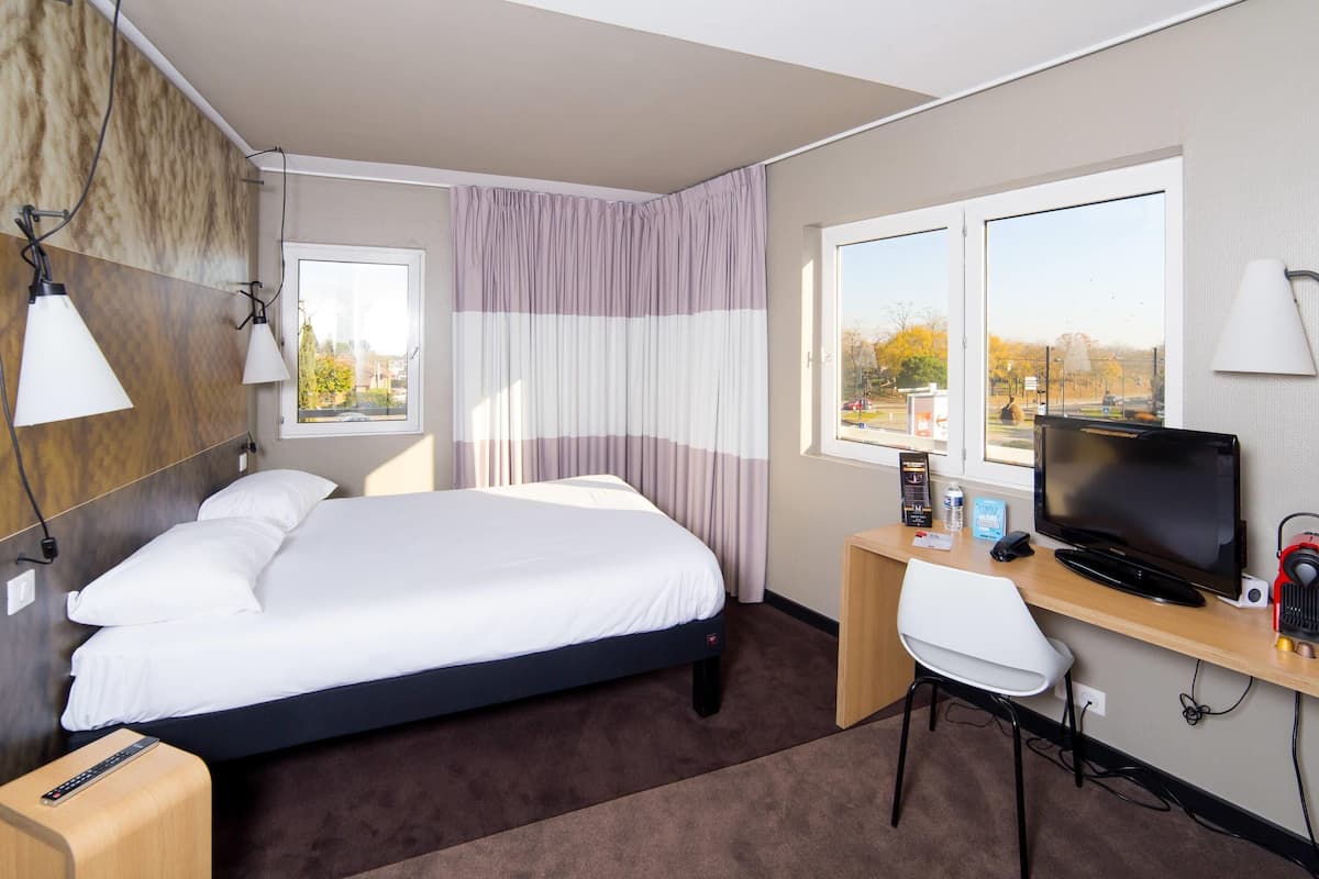 Une chambre d’hôtel équipée d’un lit, d’un bureau, d’une chaise, d’une télévision, d’une lampe et d’une fenêtre donnant sur un paysage agréable.