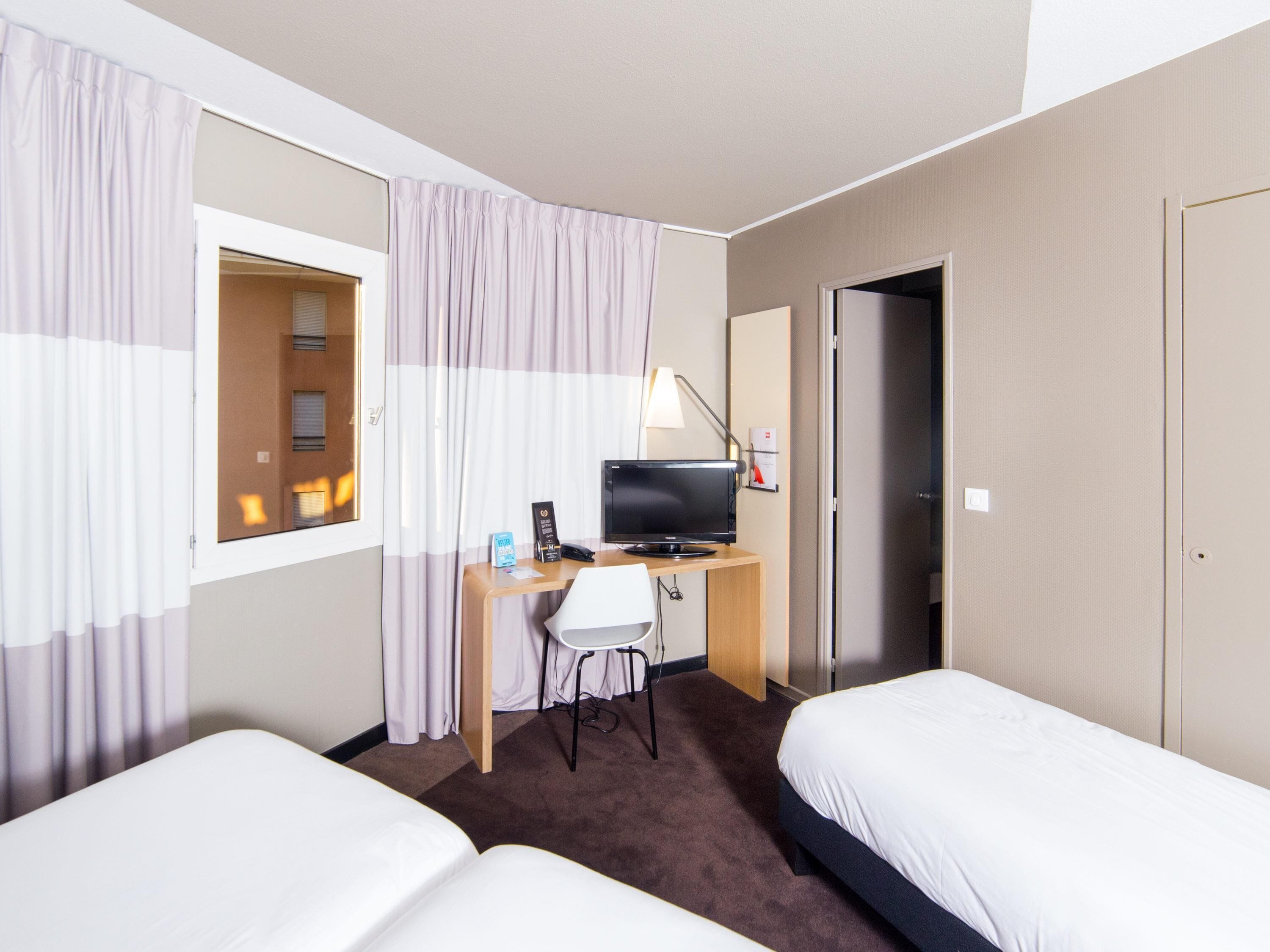 A hotel room with two beds, a desk with a computer, a chair, and a TV.