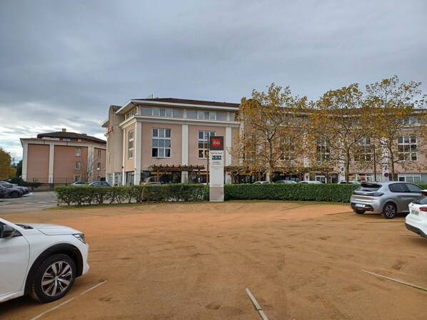 A parking lot with several cars, a building with a sign reading "Dibis," and a tree with autumn leaves.