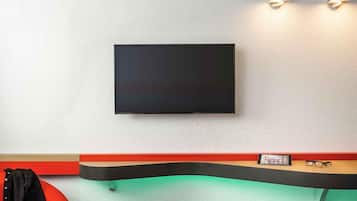 Une chambre moderne avec un téléviseur à écran plat fixé au mur, un banc rouge et noir, un petit tabouret et une paire de lunettes posées sur le banc.