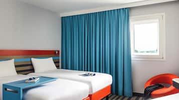 A hotel room with two beds, a window with curtains, a small table, and a chair.