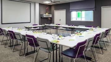 A conference room with a long table, chairs, a projector screen, ceiling fans, and a window.