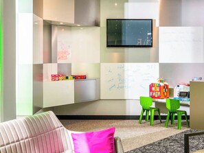 A modern room with a flat-screen TV mounted on the wall, a whiteboard with handwritten notes, and a children's play area with toys and a toy car. - ibis Styles Antony Paris Sud (Antony)