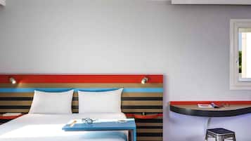 A hotel room with a bed, a bedside table, a chair, and a window.